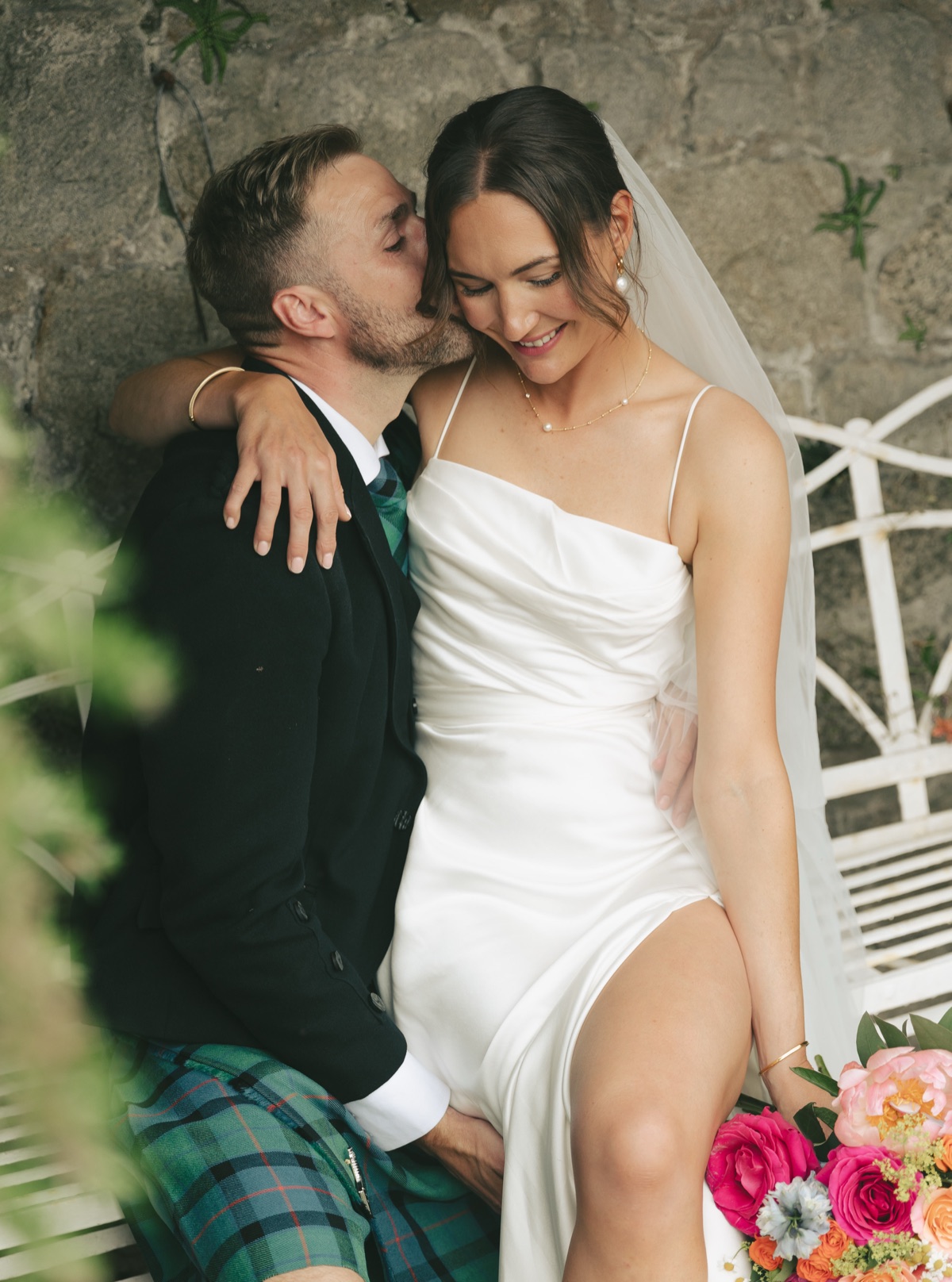 Gary kisses Isobel on the cheek as they sit together for wedding portraits in the gardens at The Dougarie Boathouse.