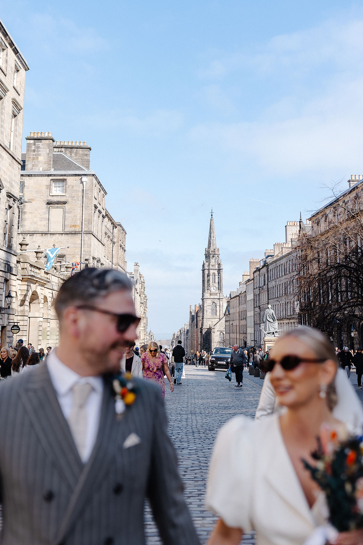 Bride and groom walk along Edinburgh’s Royal Mile after their City Chambers registry office wedding, with the city skyline and historic spire in the background.