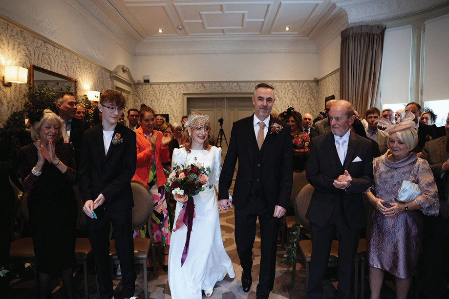 bride and groom walk up the aisle as their guests stand on either side 