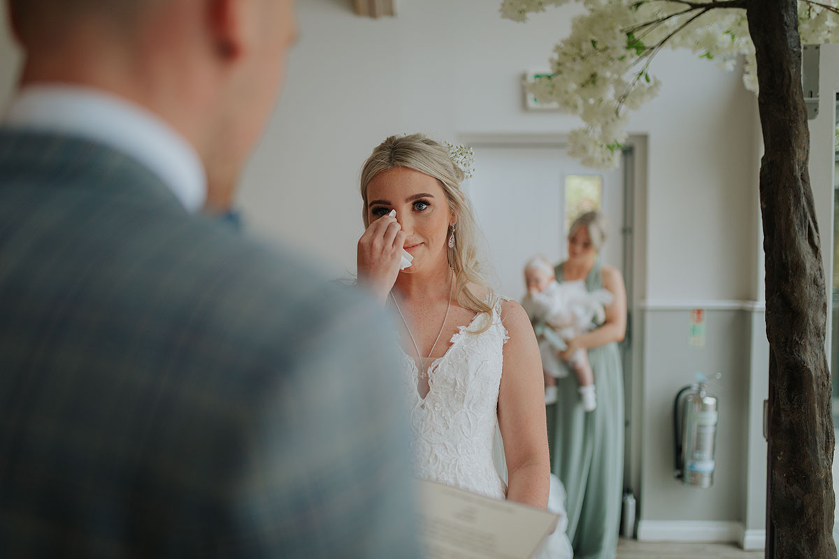 Bride Dabs A Tear Away With A Handkerchief As A Groom Reads From A Sheet Of Paper In Foreground