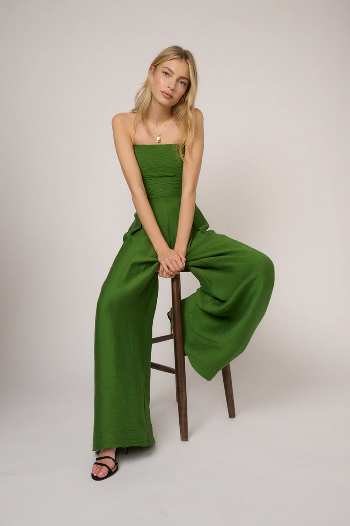 Woman wearing a strapless green wide-leg jumpsuit with a fitted bandeau bodice.