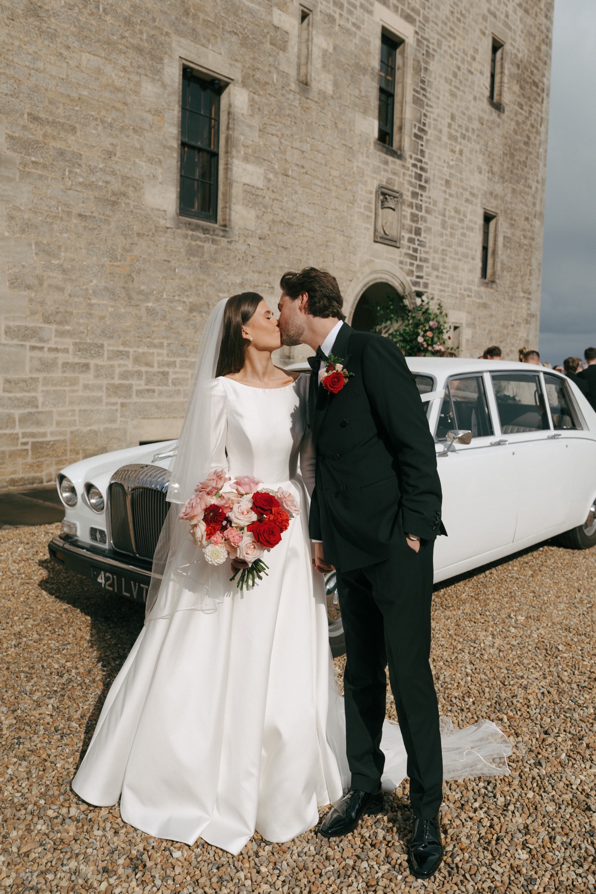 Nicole and Ryan share a kiss beside a vintage white wedding car outside Barnbougle Castle in South Queensferry.