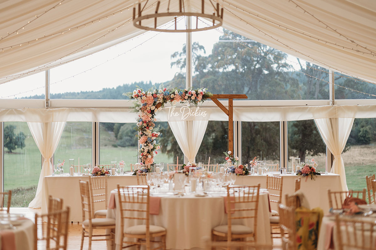 Marquee wedding reception at Ballogie House in Aberdeenshire, with pastel floral arrangements, round dining tables and a personalised floral arch behind the top table.