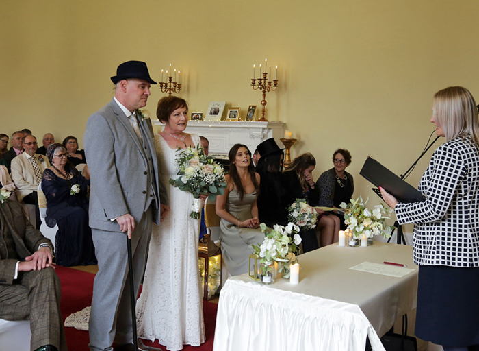 A bride and grooms stand facing the registrar during their wedding ceremony