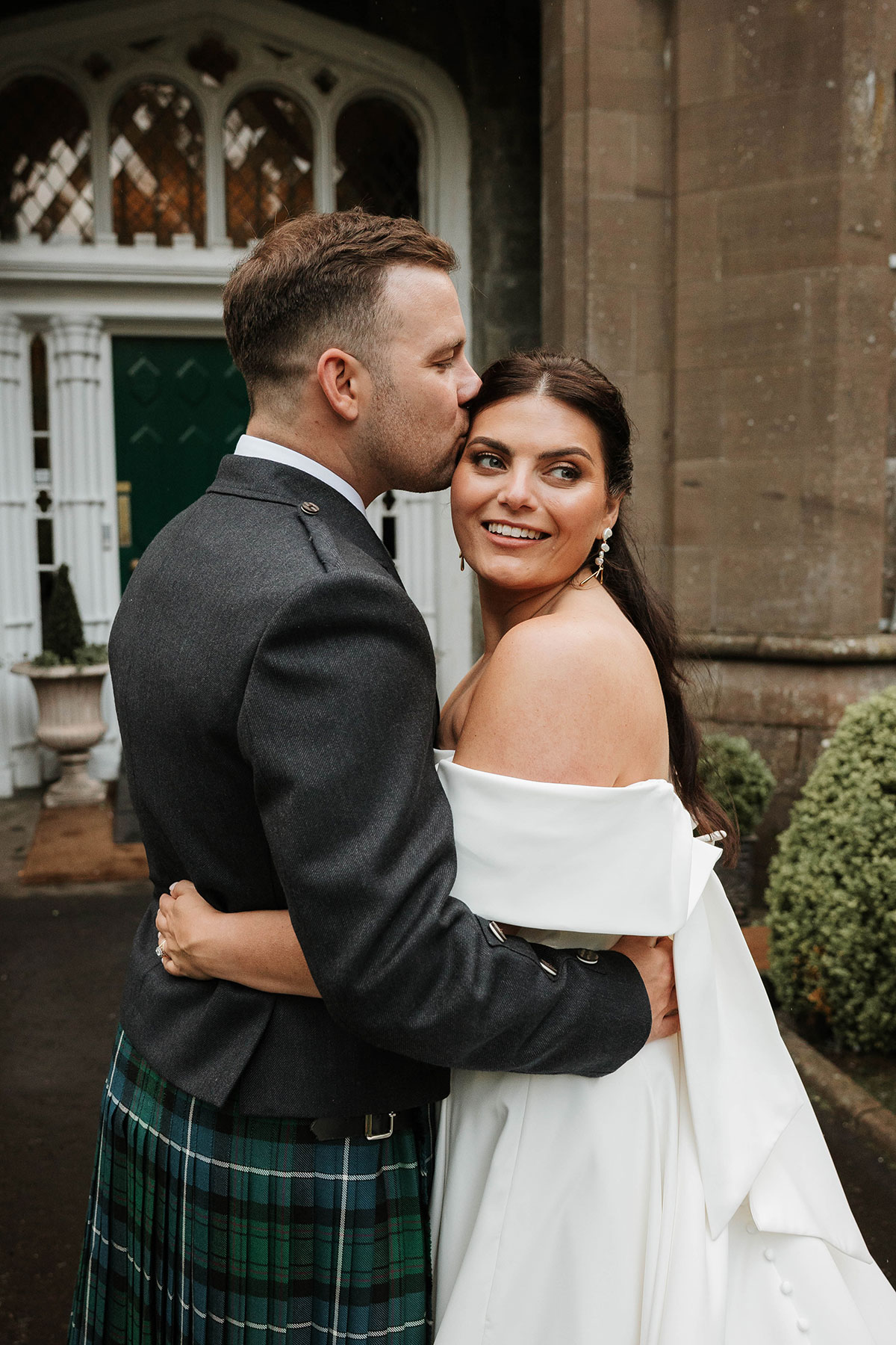 Bride and groom embracing outside Drumtochty Castle Aberdeenshire with groom kissing bride on temple