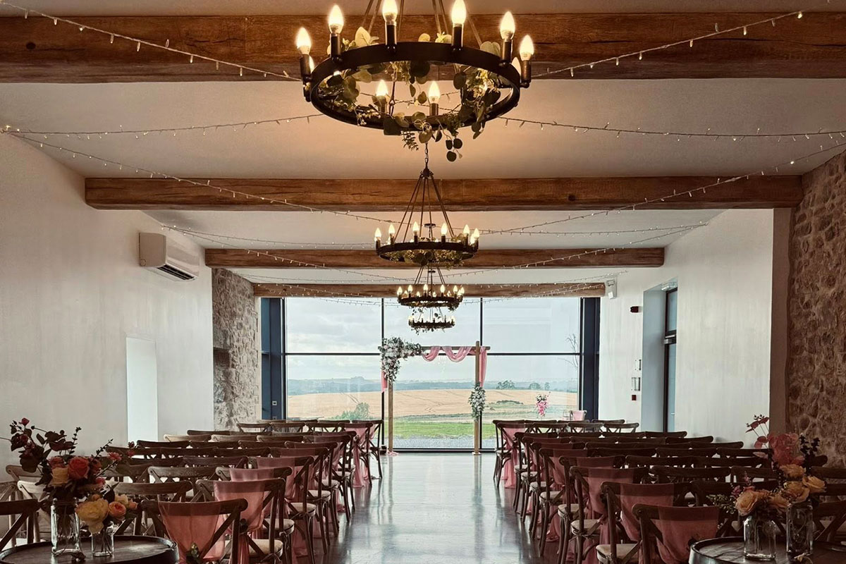 large open window overlooking fields has an altar set at the front with rows of wooden chairs with pink draping on backs of chairs lining the aisle