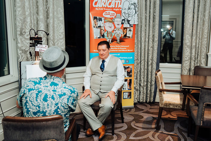 a man sitting on a chair in front of a pop up banner while he gets his caricature drawn by Edd's Heads Edd Travers