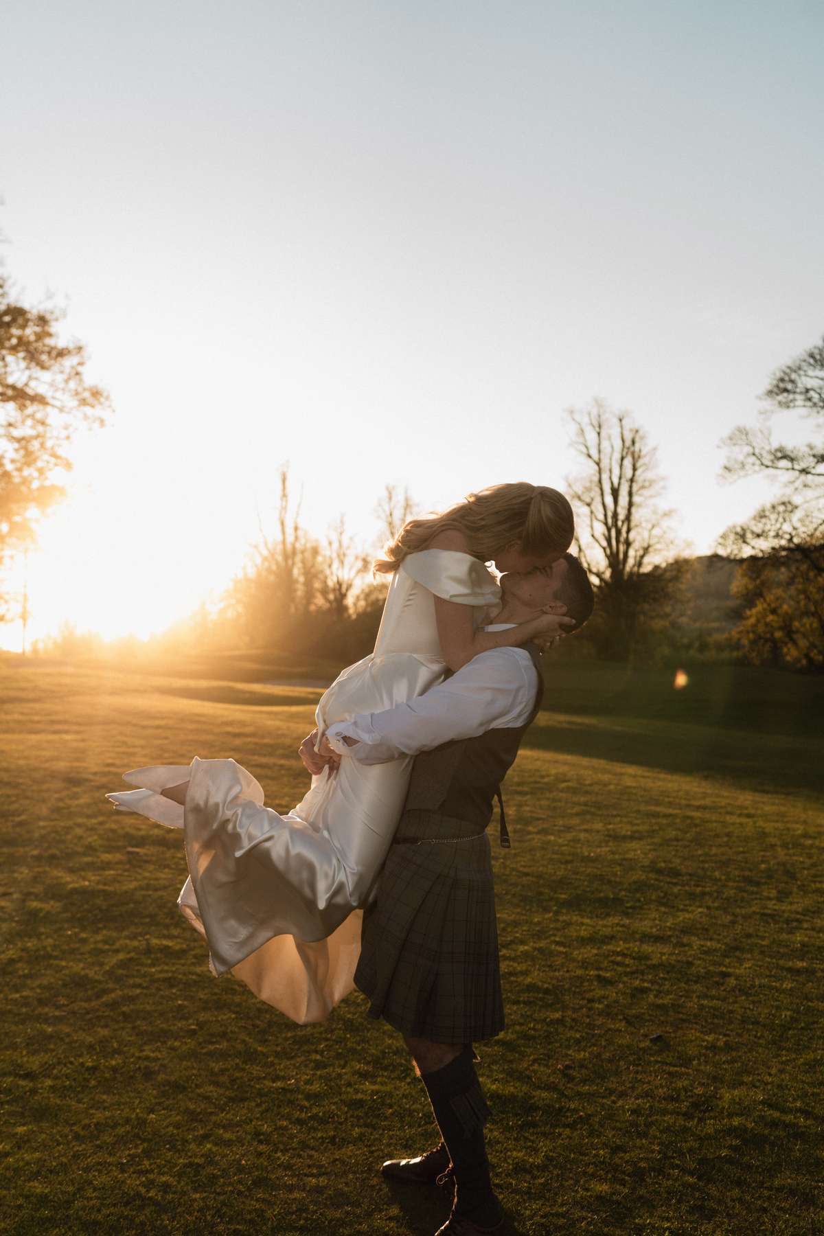 Stuart lifts Siân as the newlyweds kiss in the golden-hour sunshine in the grounds of Mar Hall.