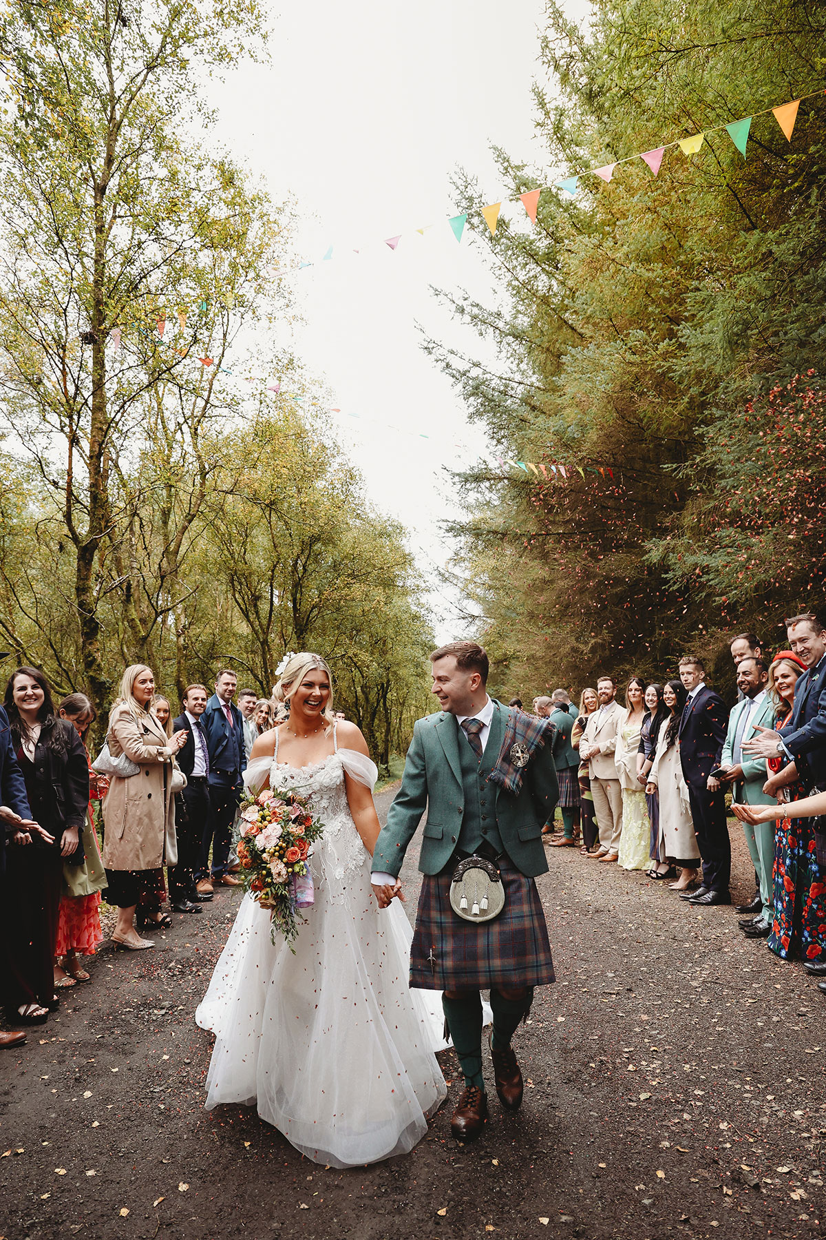 Bride and groom walking through a confetti tunnel after their outdoor woodland wedding ceremony in Scotland