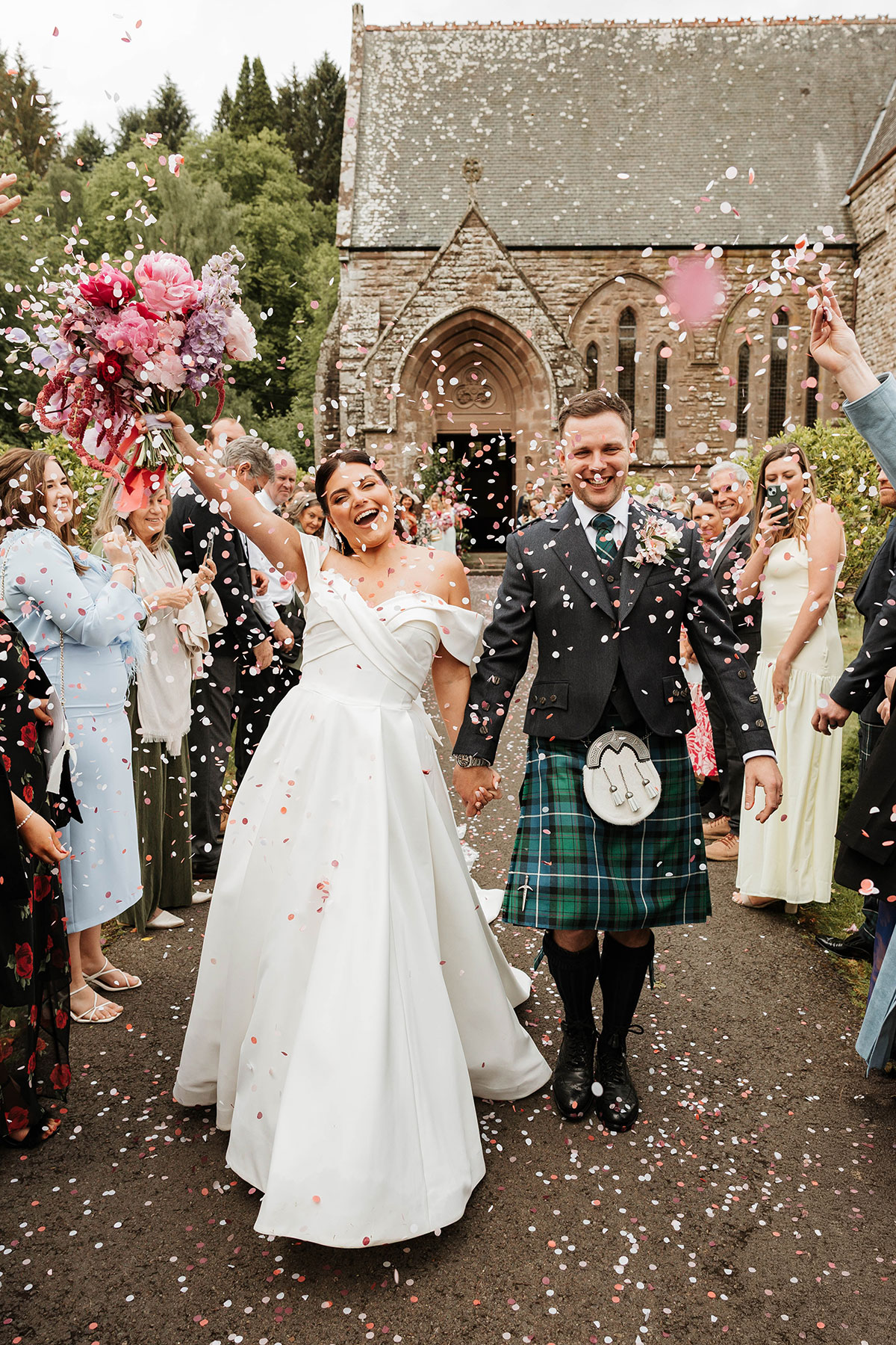 Bride and groom walking through confetti outside St Palladius Church at Drumtochty Castle Aberdeenshire wedding