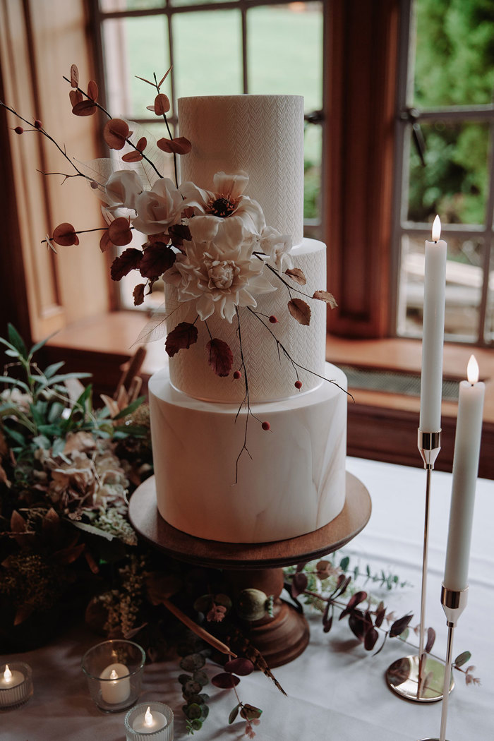 detailed marble and textured white three tier wedding cake decorated with pale pink flowers and surrounded by faux candles