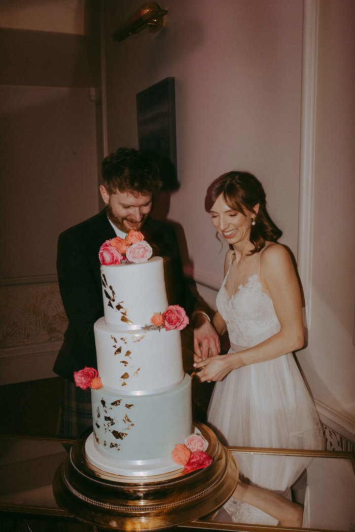 a bride and groom cutting a green and white three tier wedding cake in a pink room at Netherbyres House