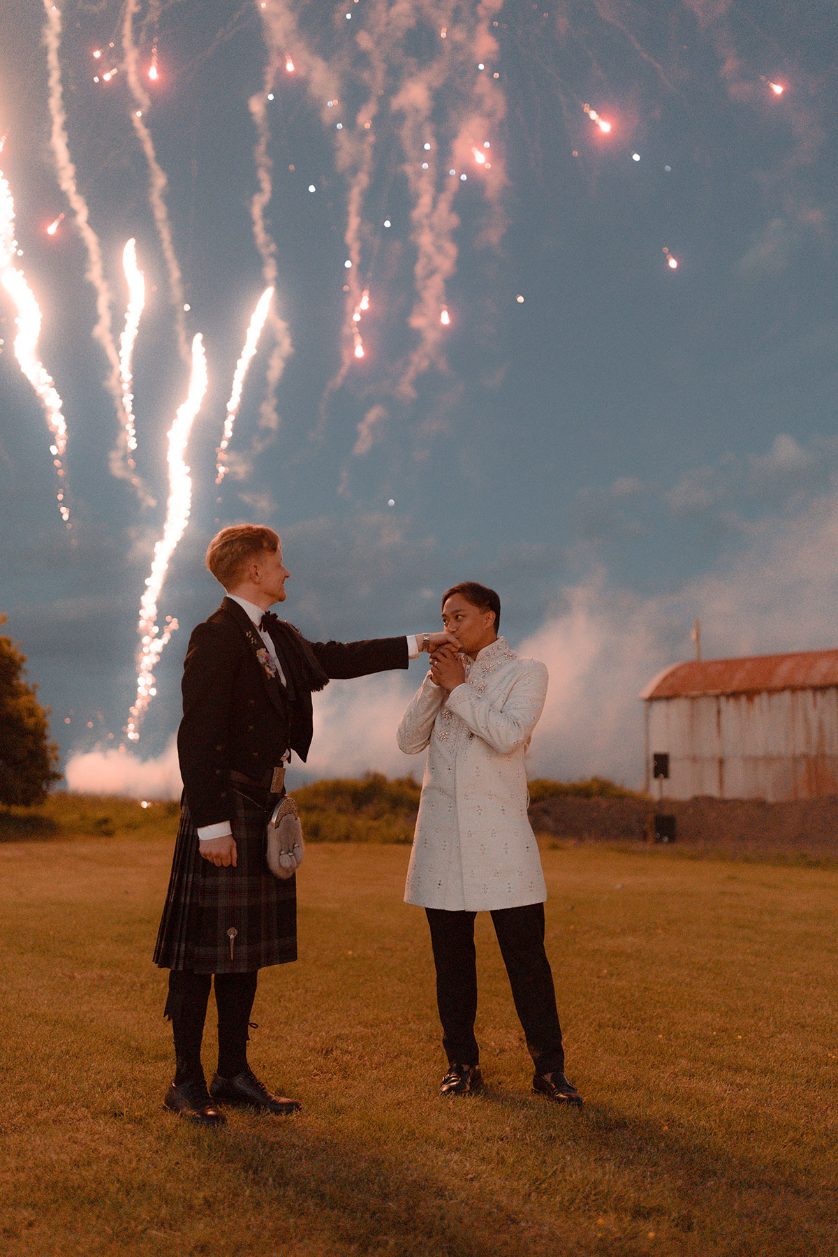 Groom kissing partner’s hand during fireworks display at intimate Scottish farm wedding