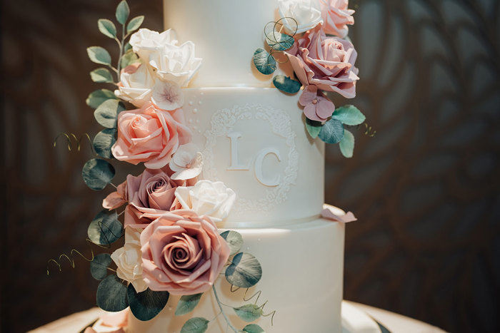 a close up of a wedding cake with pink and green flower decoration and iced L & C monogram