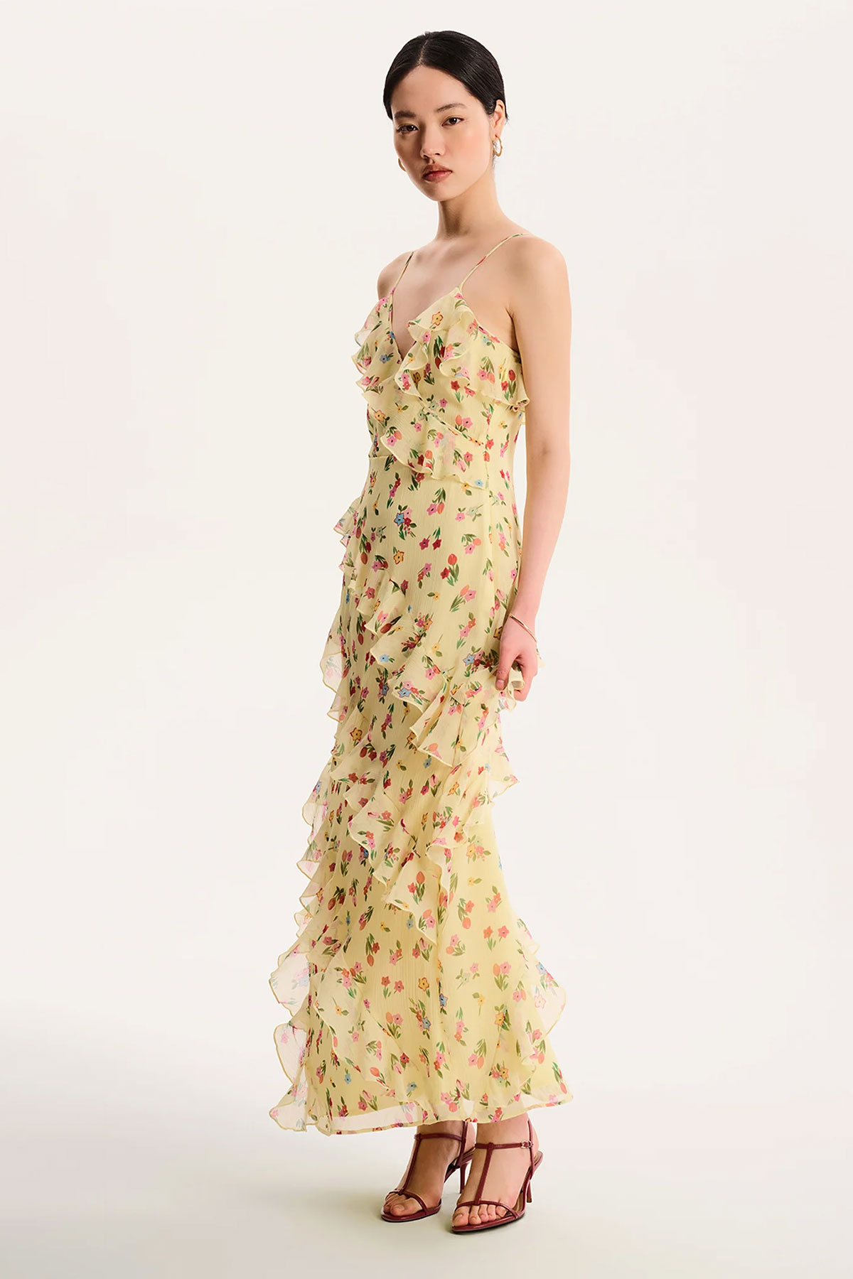 Yellow floral chiffon maxi dress with ruffle detailing and layered skirt styled with strappy heels in a studio setting