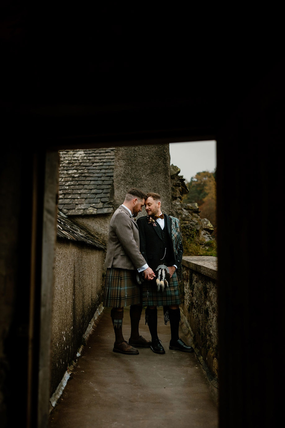 two grooms in kilts stand forehead to forehead next to a doorway in a stone building at Neidpath Castle
