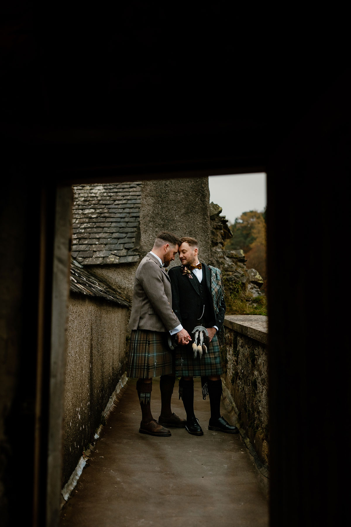 two grooms in kilts stand forehead to forehead next to a doorway in a stone building at Neidpath Castle