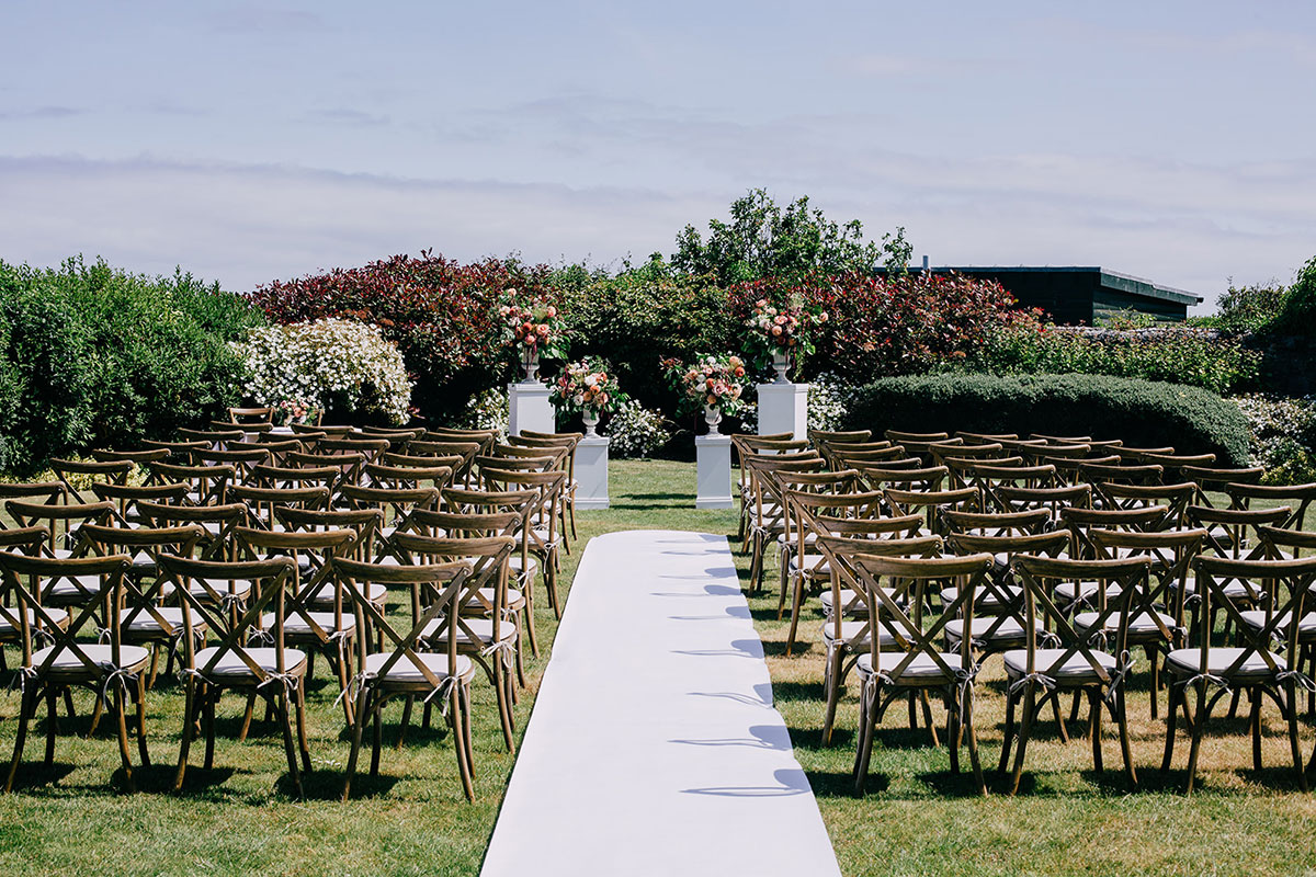 Outdoor wedding ceremony setup with wooden chairs and floral arrangements in a walled garden