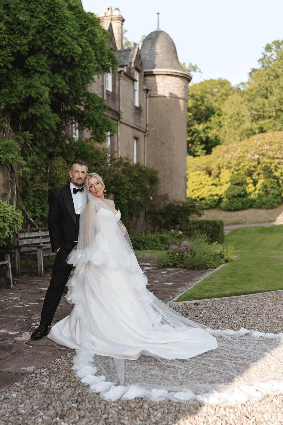 Stylish bride and groom posing outside a Scottish castle wedding venue, featuring a statement ruffled wedding dress and classic black tuxedo styling