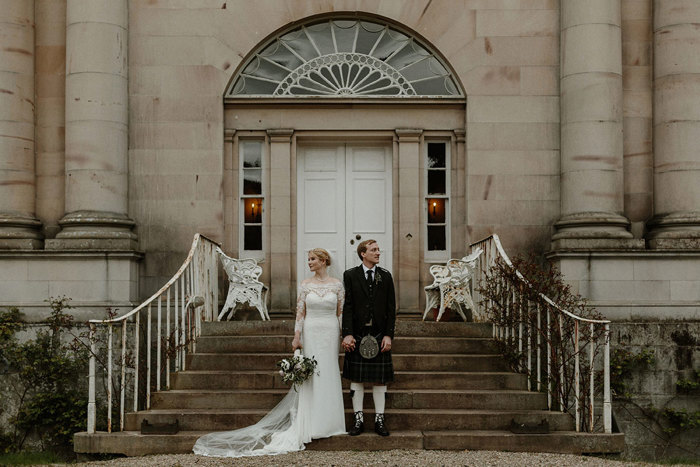 bride and groom stand on steps holding hands in front of the byre at inchyra's house