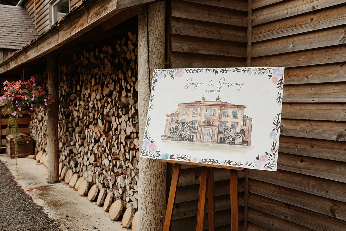 a painted wedding welcome sign on an easel next to a wood shed at Netherdale House