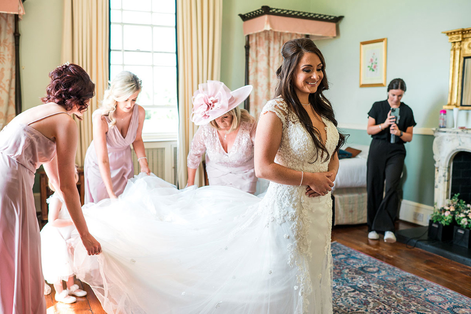 Bride is helped with her dress by bridesmaids and mum