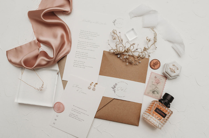 Flat lay image of white- and blush-coloured items including perfume and stationery 