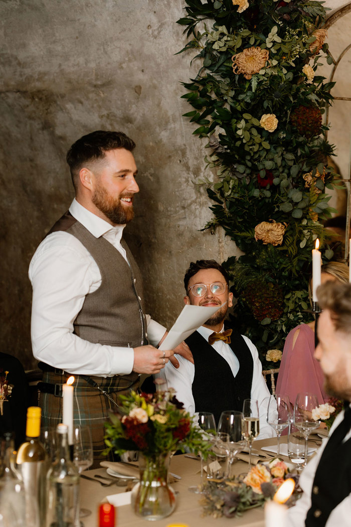a groom standing holding a sheet of paper during a wedding reception at Neidpath Castle