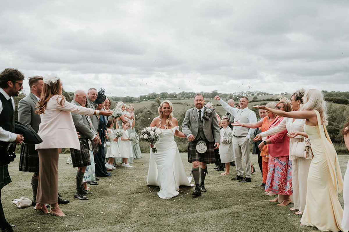 Bride and groom walking through guests throwing confetti at Eden Leisure Village countryside wedding venue.