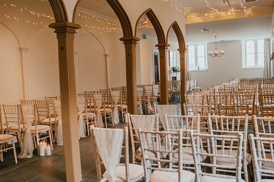 inside a wedding ceremony room with white chivari chairs and fairy lights