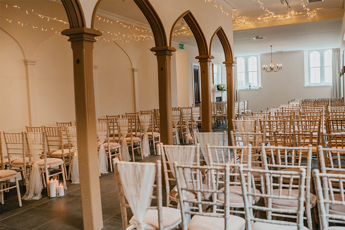 inside a wedding ceremony room with white chivari chairs and fairy lights