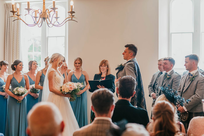 A wedding ceremony with the bride, groom, officiant, bridesmaids and groomsmen standing in from of the guests