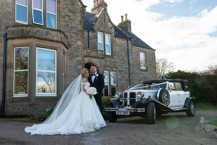 A Bride And Groom Standing With A Vintage Car Ourside A Country House Hotel In The Highlands