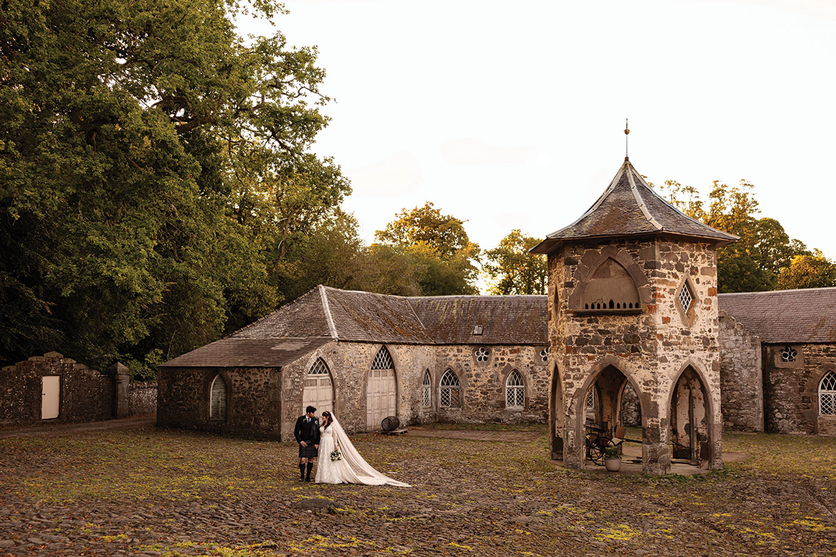 Newlywed couple posing outside a historic stone Scottish wedding venue in warm evening light.