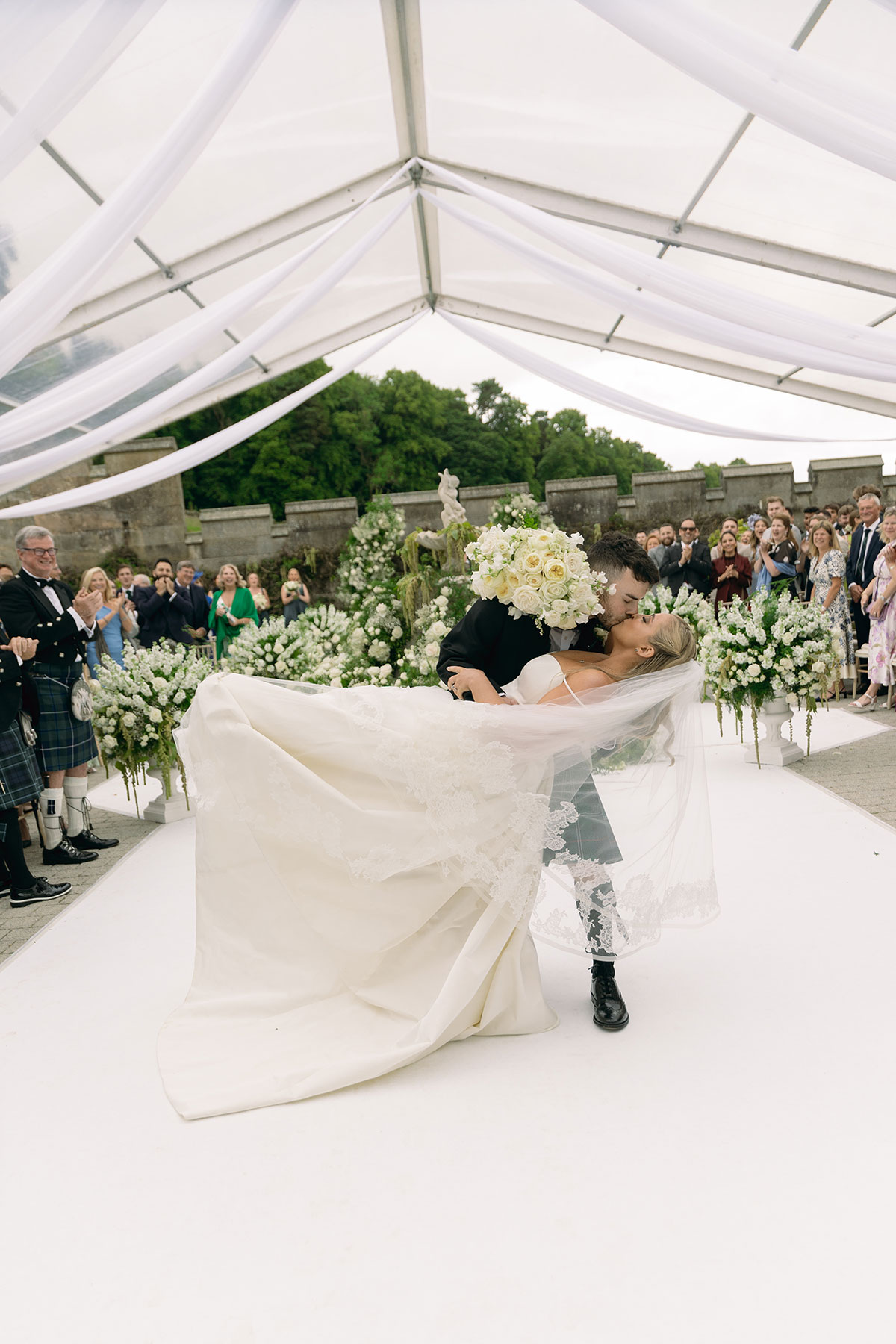 Newlyweds share a dramatic dip kiss beneath floral arch after outdoor ceremony at Dundas Castle.