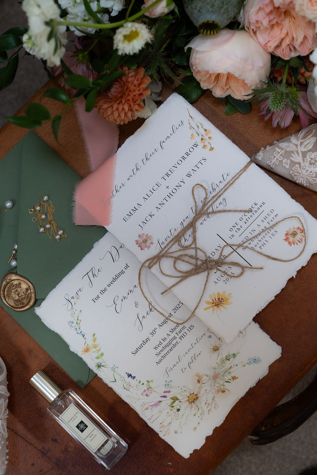 Wedding stationery flat lay with handmade invitations, wax seal, perfume and peach floral styling