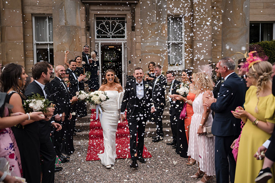 Bride and groom walking through confetti with guests celebrating around them