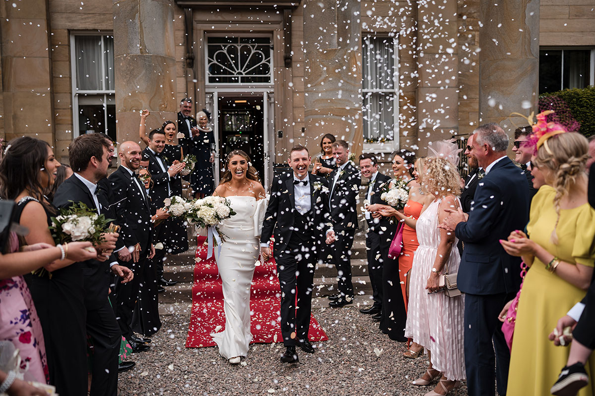 Bride and groom walking through confetti with guests celebrating around them