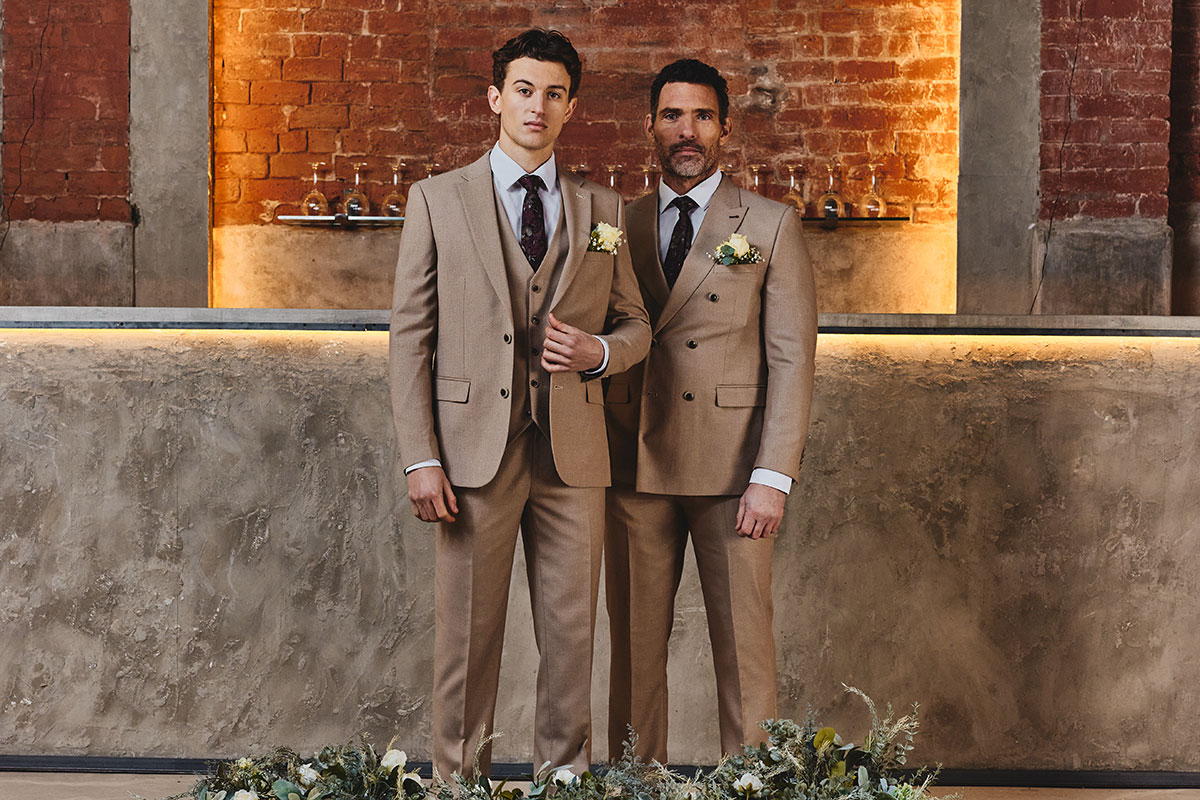 Two men standing in beige suits surrounded by flower decor
