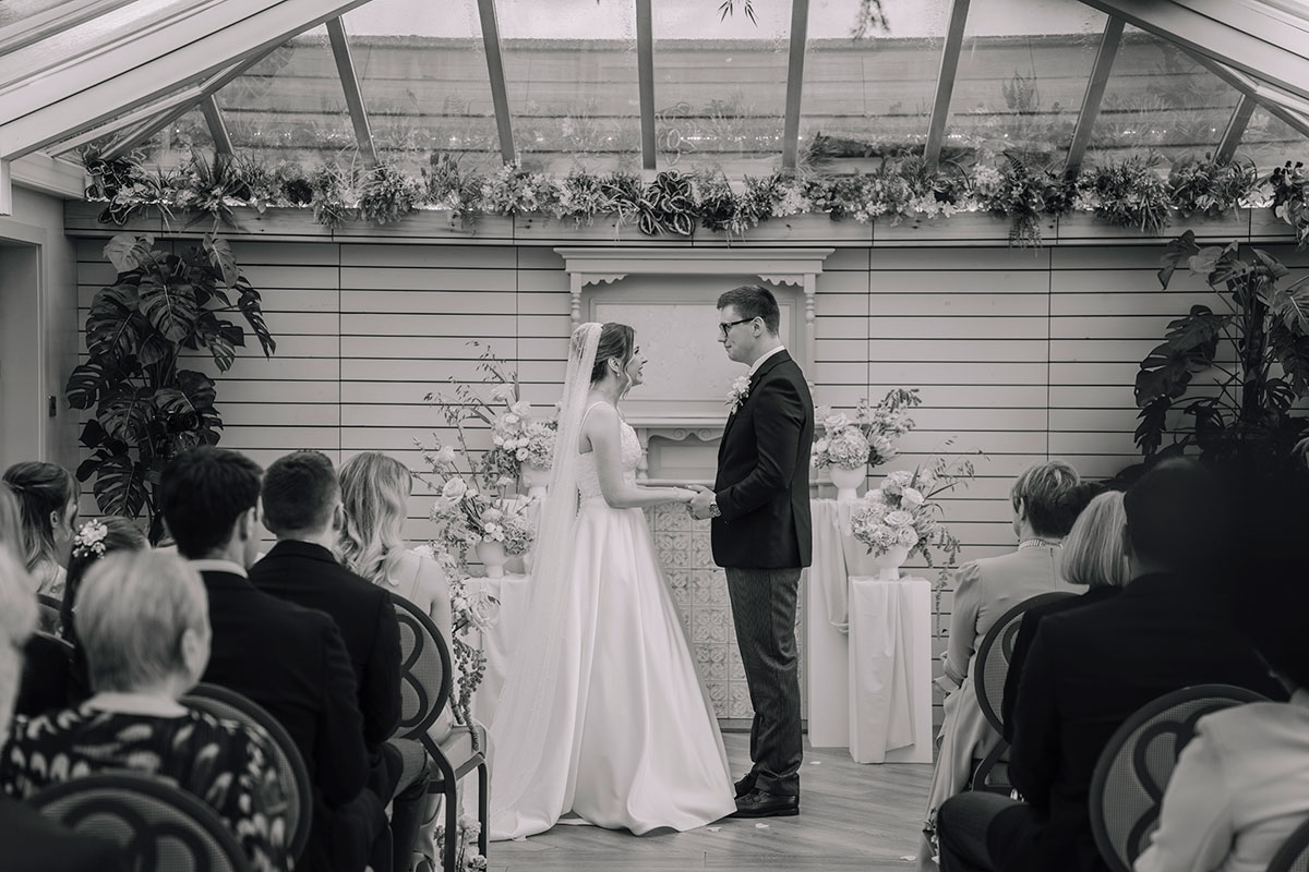 Bride and groom exchanging vows during a romantic indoor wedding ceremony with floral arrangements and guests seated