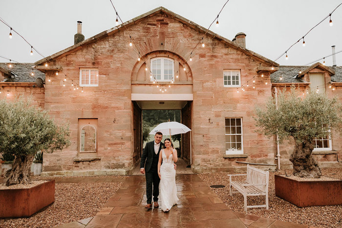 a bride and groom in the courtyard at Dunglass Estate under an ivory umbrella