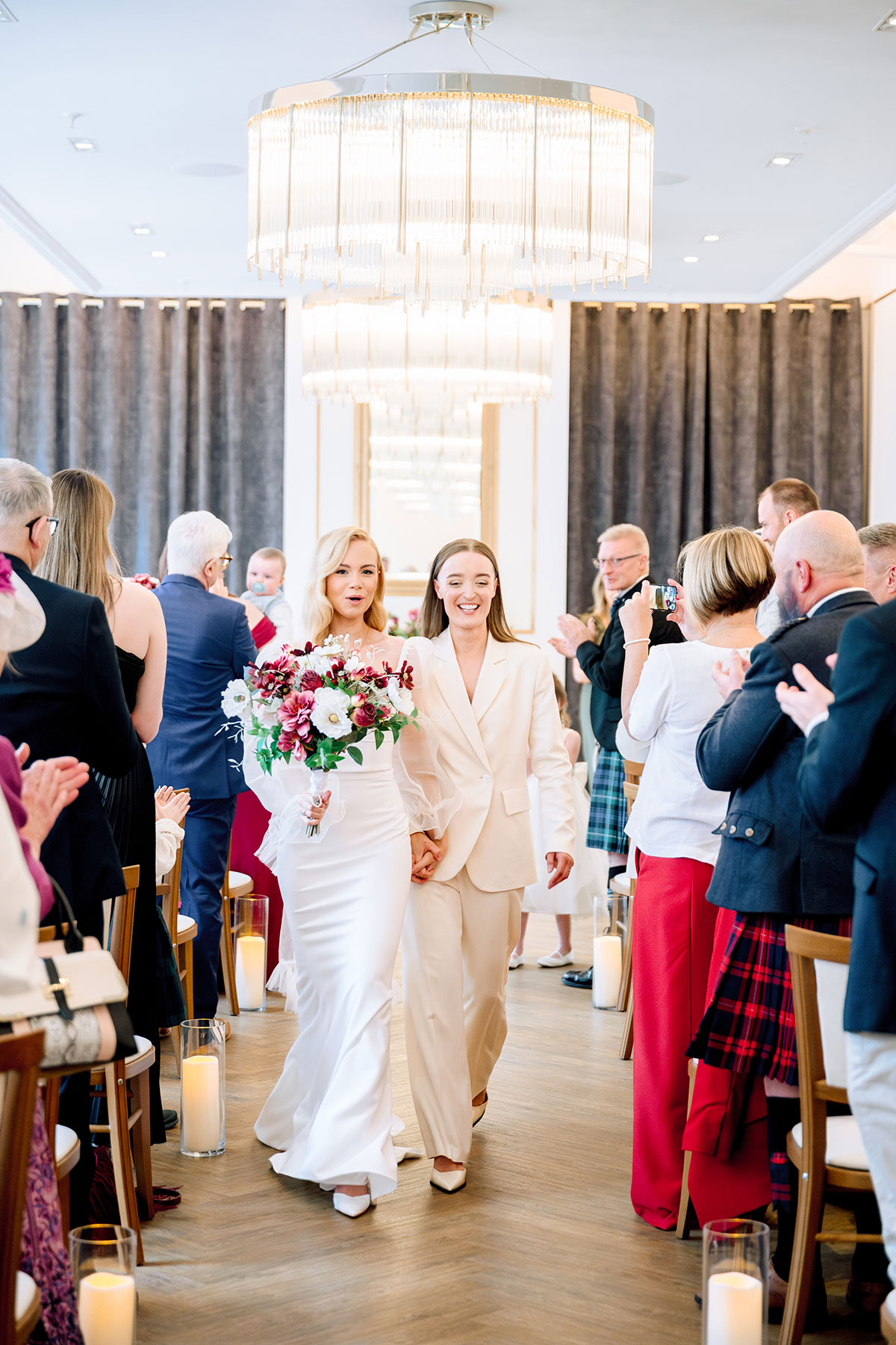 Just married brides walking up the aisle holding hands.