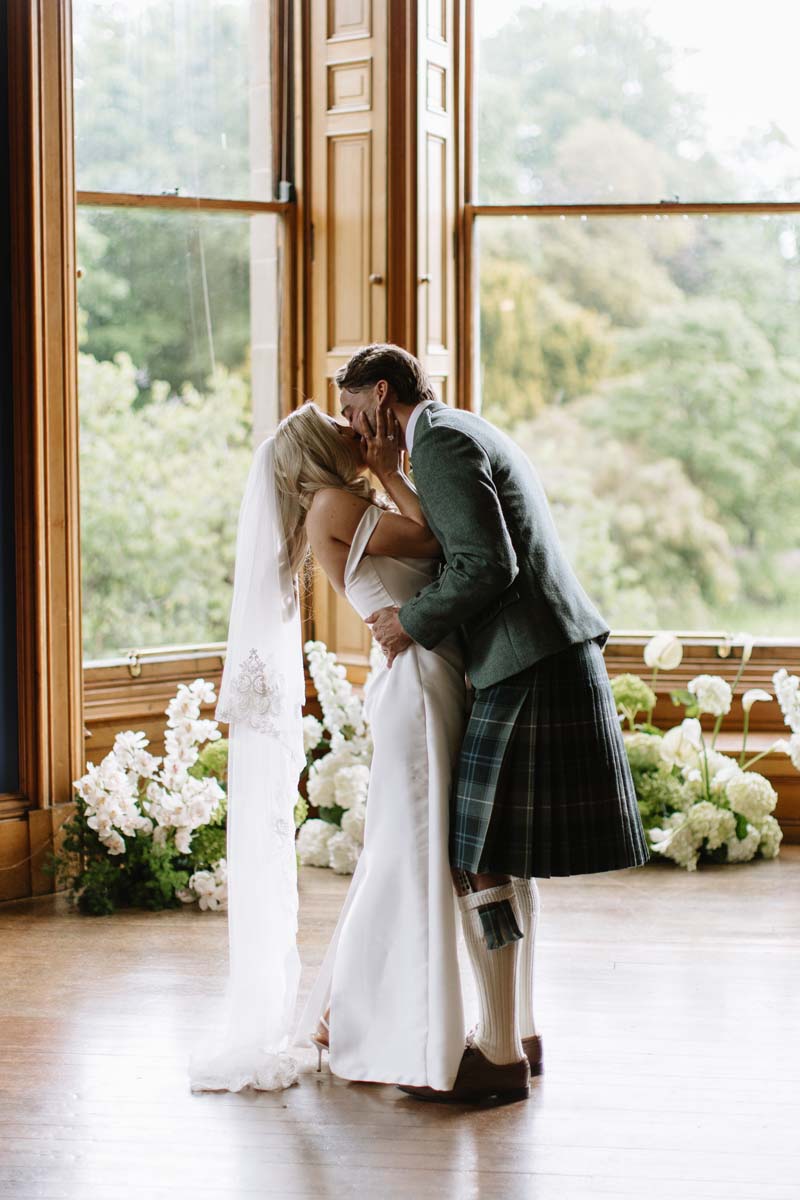 Lia and Louis share their first kiss as newlyweds following their wedding ceremony in the library at Cambo House