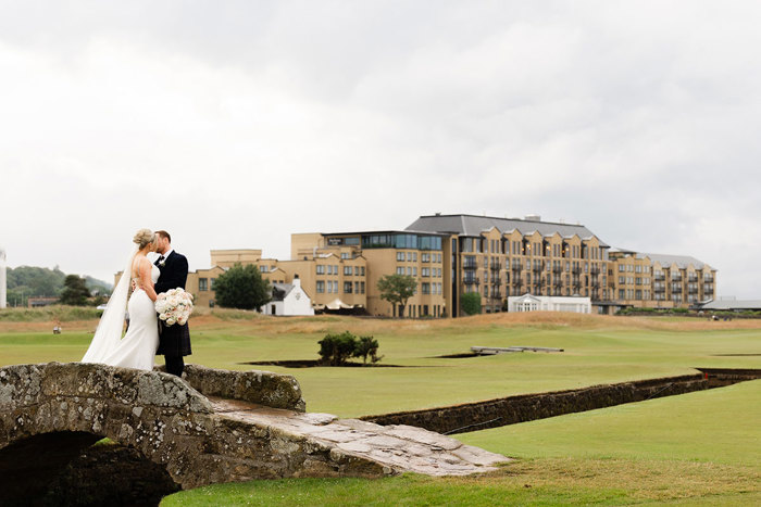 a bride and groom kiss on Swilcan Bridge with Old Course Hotel in background