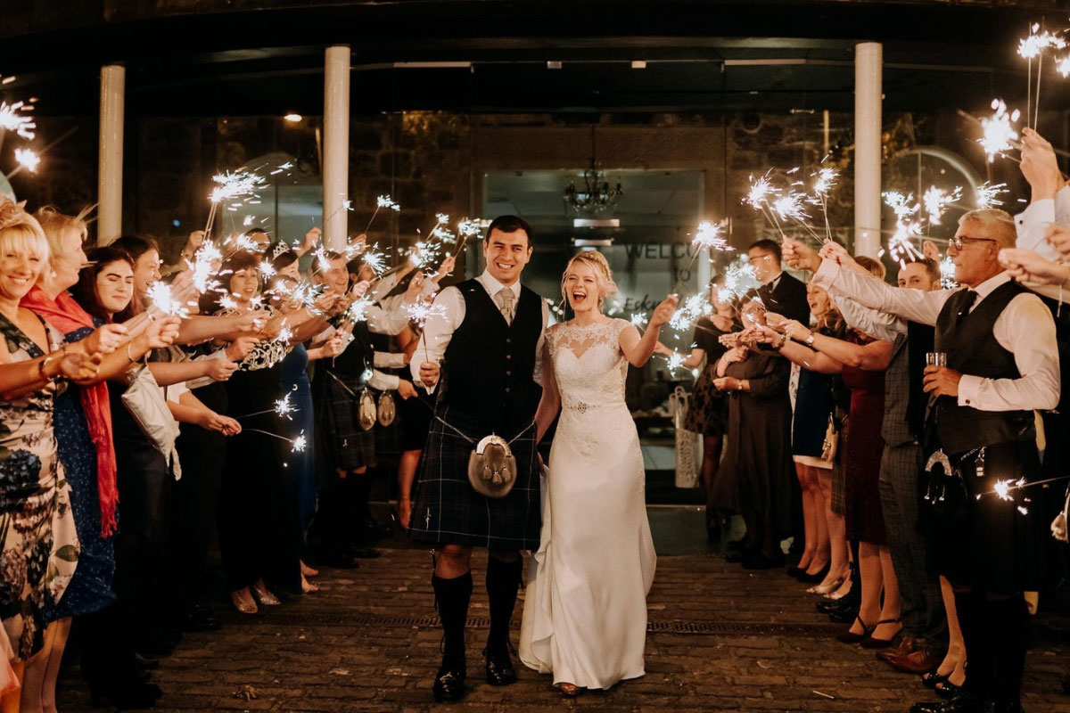 a bride and groom surrounded by their wedding guests all holding sparklers to create a glow against the night sky
