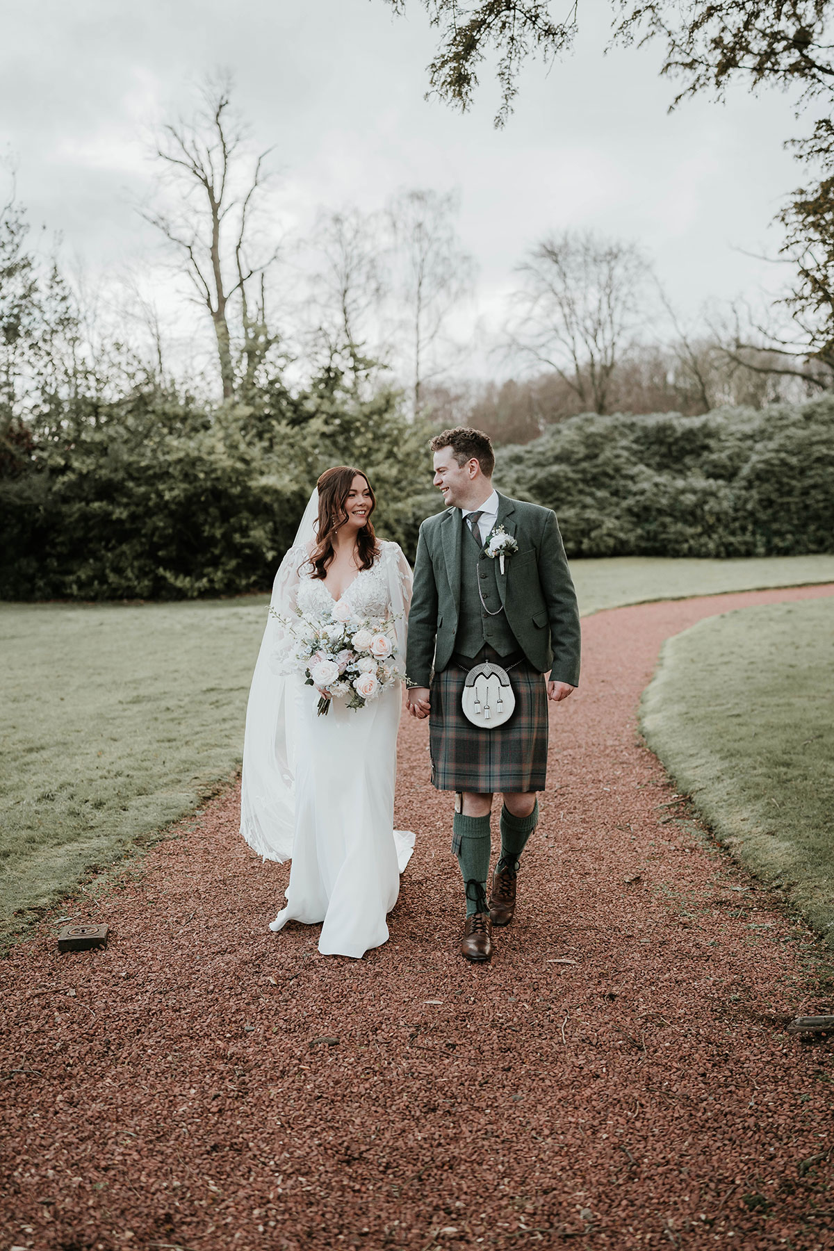 Bride and groom walking through the gardens of Norton House, smiling at each other