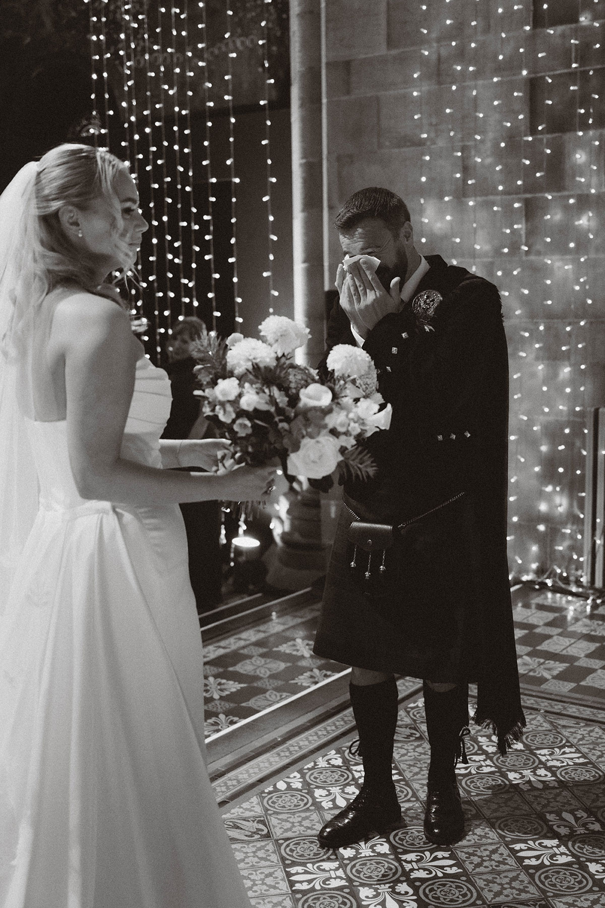 groom wiping tears during emotional wedding ceremony with bride holding bouquet