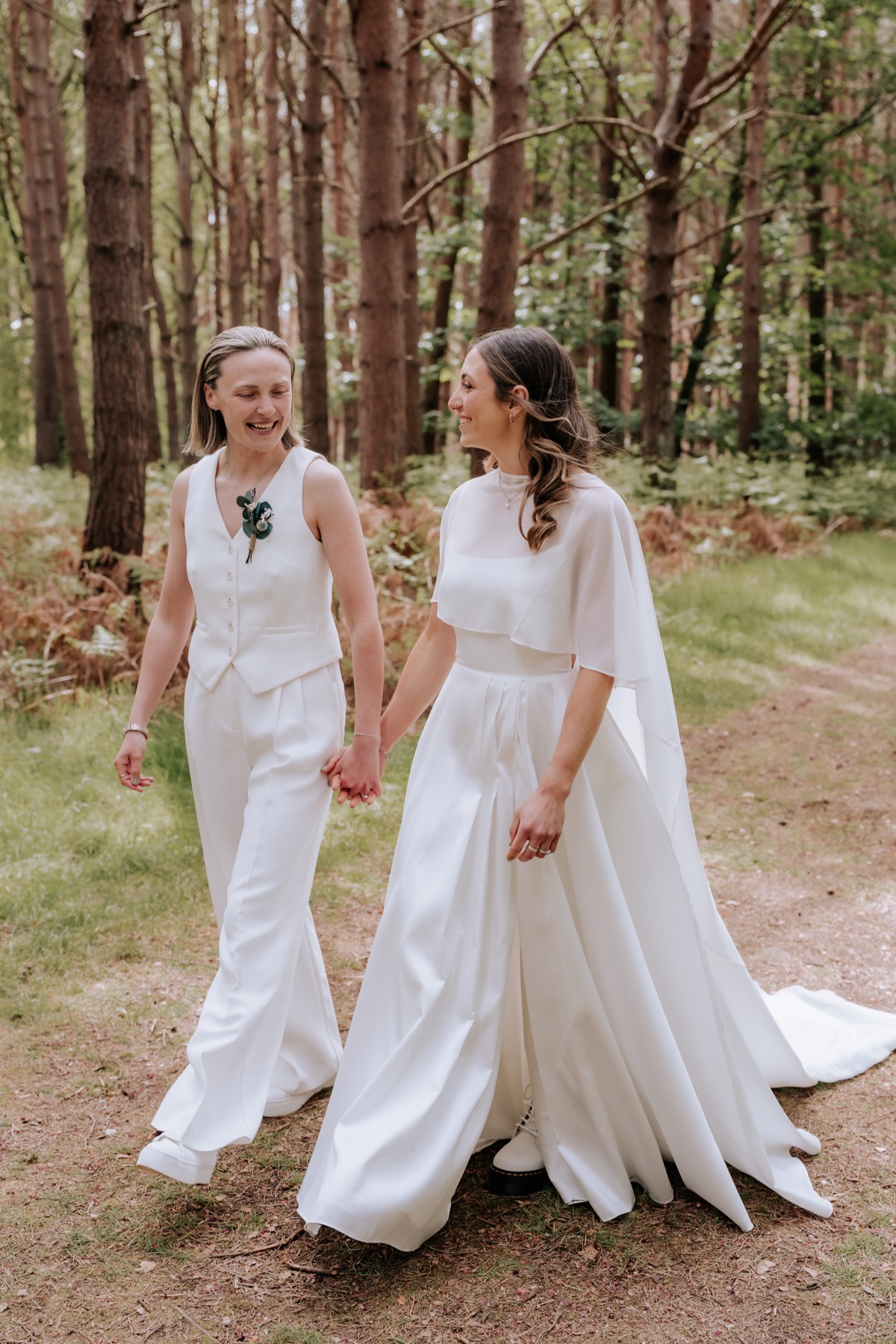 Hannah and Donna walking hand in hand through the woodland at Harvest Moon on their wedding day.
