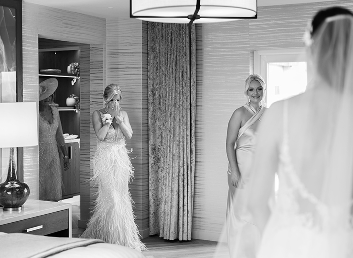 a black and white image of a person wearing a fringed evening gown holding hands up to face in surprise as they look at a bride