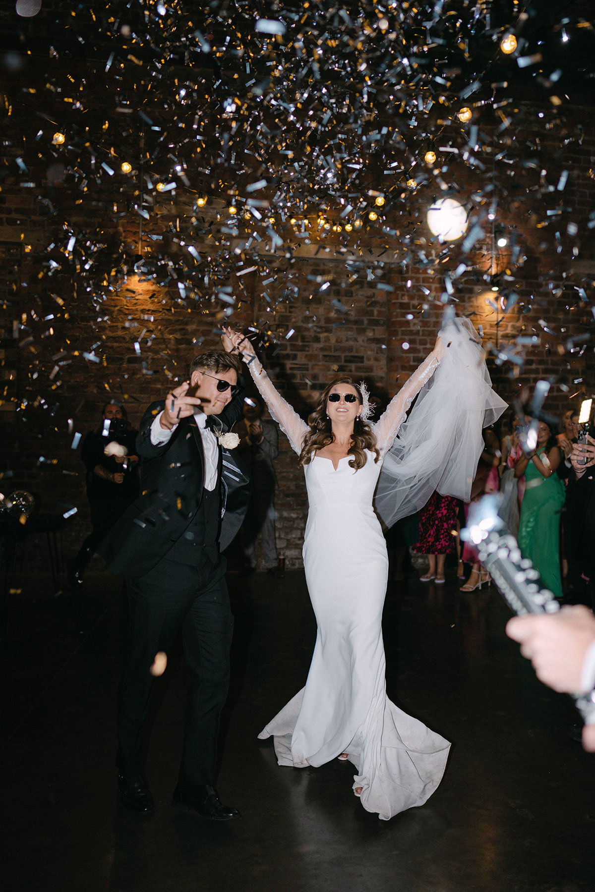 Newly married couple wearing sunglasses and dancing through a shower of confetti during their wedding reception entrance.